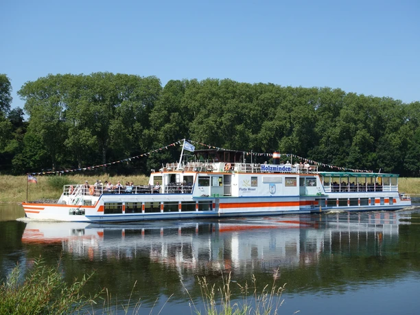 Flotte Weser Das Ausflugsschiff Flotte Weser fährt auf einem Fluss, gesäumt von grünen Bäumen.