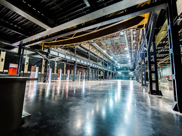 Palladium Köln Haupthalle Die Haupthalle des Palladiums in Köln präsentiert sich als beeindruckende, weitläufige industrielle Veranstaltungsfläche mit glänzendem Boden und einer hohen Stahlkonstruktion, die offene Sicht auf die Dachstruktur bietet.