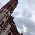Roof gallery of the Alte Nikolaikirche Church tower with colorful balloons on the railing under a cloudy sky.