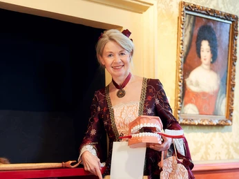 Kammerfrau Juliette: Historische Kostümführung im Celler Schloss Gästeführerin als Kammerfrau Juliette in historischem Kostüm hält ein Modell von Zähnen und zeigt auf ein Bild in einem Schrank.