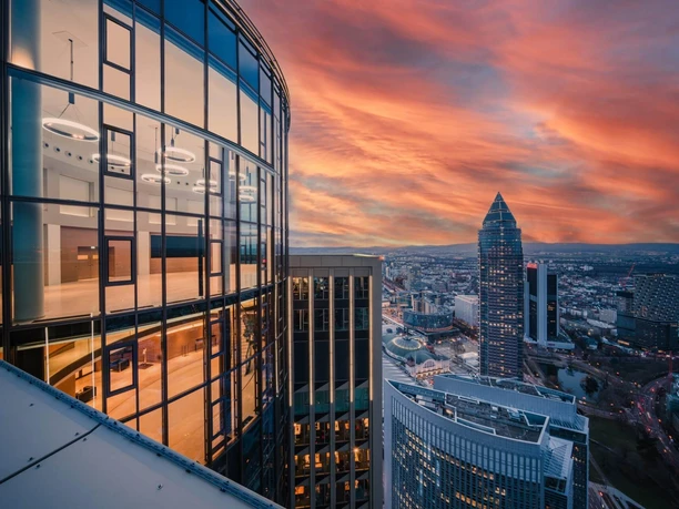TOWER185/FIFTY HEIGHTS Glasfassade eines Hochhauses mit Blick auf Frankfurts Skyline bei Sonnenuntergang.