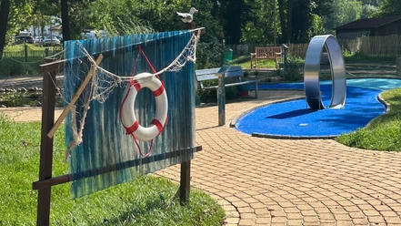 Adventuregolf am Meer Ein kurviger, gepflasterter Weg führt zu einer modernen Adventuregolfanlage, umgeben von Bäumen.