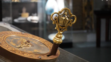 Blick in die Ausstellung Uhrenschloss Ein kunstvoller Schlüssel mit goldenen Verzierungen und detaillierten Ornamenten in einer Vitrine.