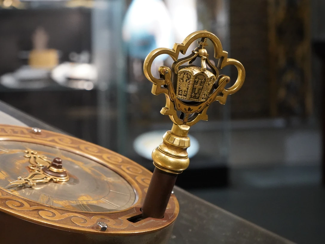 Blick in die Ausstellung Uhrenschloss Ein kunstvoller Schlüssel mit goldenen Verzierungen und detaillierten Ornamenten in einer Vitrine.