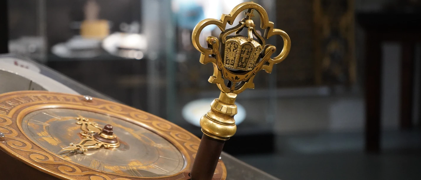 Blick in die Ausstellung Uhrenschloss Ein kunstvoller Schlüssel mit goldenen Verzierungen und detaillierten Ornamenten in einer Vitrine.