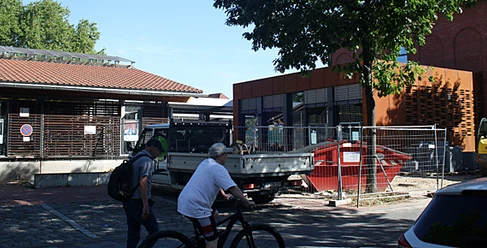 Zwei Personen mit Fahrrädern vor modernem Gebäudeensemble am Bahnhof Bünde bei sonnigem Wetter.