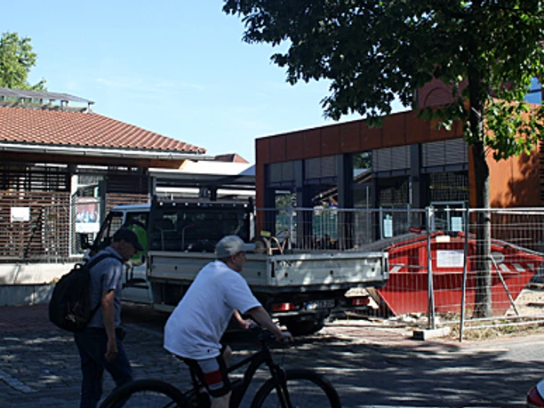 bünde-bahnhof-foto.jpg Zwei Personen mit Fahrrädern vor modernem Gebäudeensemble am Bahnhof Bünde bei sonnigem Wetter.