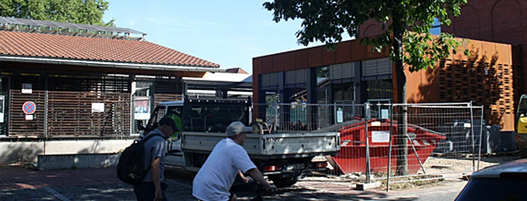 bünde-bahnhof-foto.jpg Zwei Personen mit Fahrrädern vor modernem Gebäudeensemble am Bahnhof Bünde bei sonnigem Wetter.