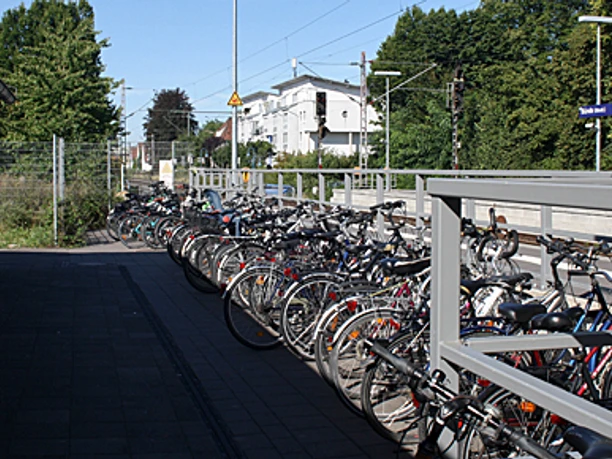 Viele Fahrräder sind nebeneinander an einem Bahnhof in Bünde, umgeben von Bäumen, abgestellt.
