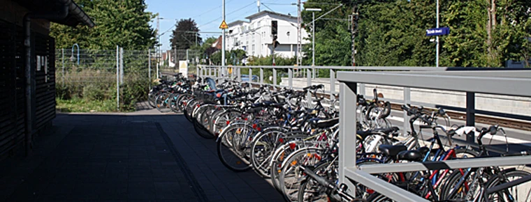 bahnhof-bünde-fahhrad.jpg Viele Fahrräder sind nebeneinander an einem Bahnhof in Bünde, umgeben von Bäumen, abgestellt.