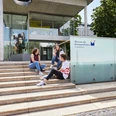 Außenansicht des Museums für Kommunikation Frankfurt mit Jugendlichen auf der Treppe Drei Jugendliche sitzen entspannt auf den Treppen vor dem modernen Eingangsgebäude des Museums für Kommunikation Frankfurt.Three young people sitting relaxed on the stairs in front of the modern entrance building of the Museum of Communication Frankfurt.