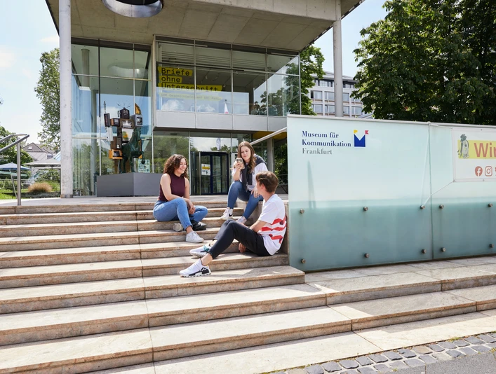 Außenansicht des Museums für Kommunikation Frankfurt mit Jugendlichen auf der Treppe Drei Jugendliche sitzen entspannt auf den Treppen vor dem modernen Eingangsgebäude des Museums für Kommunikation Frankfurt.Three young people sitting relaxed on the stairs in front of the modern entrance building of the Museum of Communication Frankfurt.