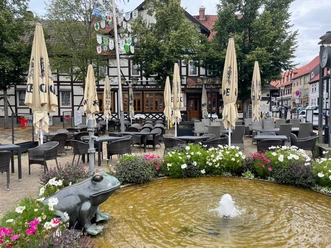 hackepeter.jpg Im Vordergrund ist ein Brunnen mit einer Froschstatue, dem Ütschenpaul, zu sehen und dahinter das Restaurant Hackepeter mit seinem Außensitzbereich. Die Tische sind noch leer und die Sonnenschirme geschlossen.