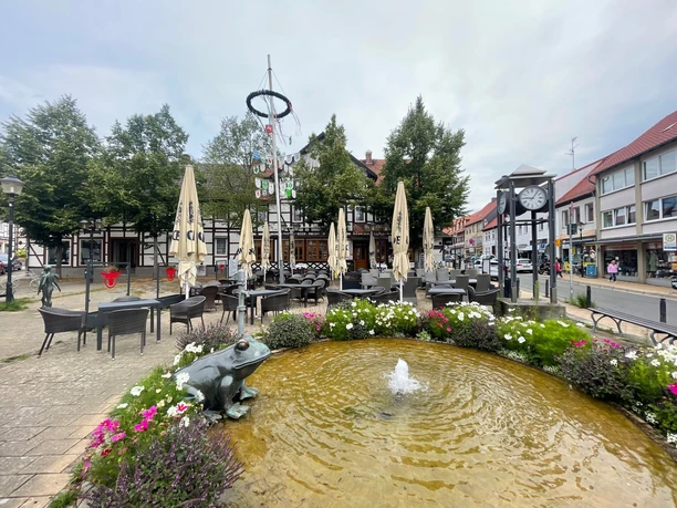 hackepeter2.jpg Im Vordergrund ist ein Brunnen mit einer Froschstatue, dem Ütschenpaul, zu sehen und dahinter das Restaurant Hackepeter mit seinem Außensitzbereich. Die Tische sind noch leer und die Sonnenschirme geschlossen.