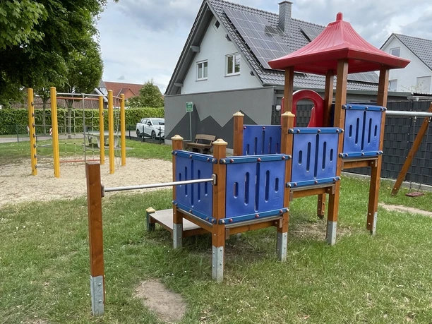 Uppen Brinke Das Bild zeigt einen Spielplatz mit Klettergerüst, Schaukeln und einem kleinen Spielhaus auf einer Wiese.