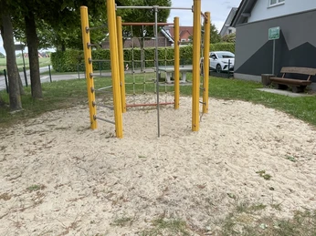 Das Bild zeigt ein Klettergerüst auf einem Spielplatz. Es ist umgeben von Rasen und Bäumen.