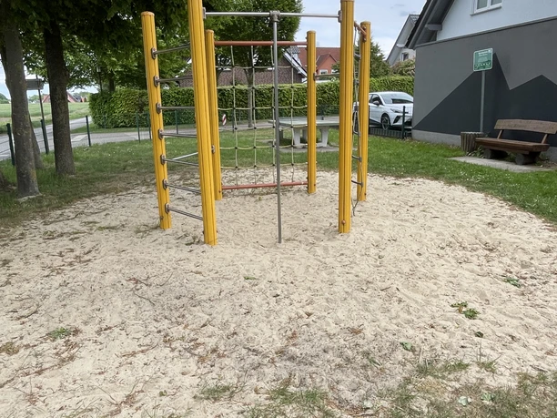 Uppen Brinke Das Bild zeigt ein Klettergerüst auf einem Spielplatz. Es ist umgeben von Rasen und Bäumen.