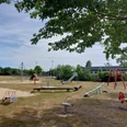 Der Spielplatz mit Rutschen, Schaukeln und Wippen lädt zum Spielen ein. Schatten spendet ein Baum.