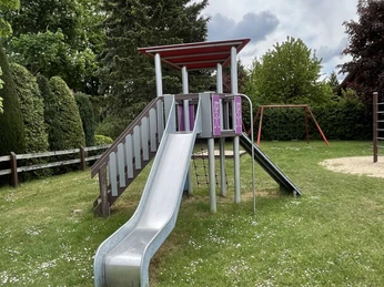 Eine Rutsche und eine Treppe stehen auf einem grünen Rasen mit verstreuten Gänseblümchen.