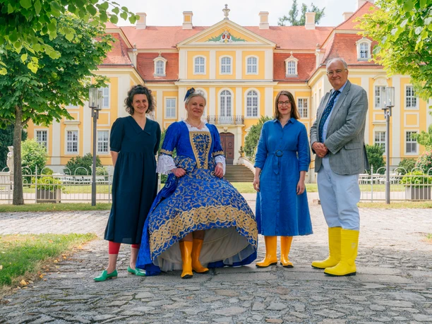 Presseevent-Neueroeffnung-Rammenau_c_Schloesserland-Sachsen-Alexander-Gentzel-1115.jpg Vier Personen stehen vor einem Schloss in bunter Kleidung und gelben Gummistiefeln.