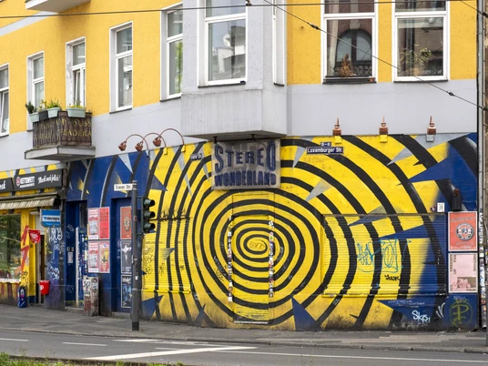 Stereo Wonderland Bunte Graffiti mit Spiralmotiv ziert eine Hauswand, belebt von urbanen Aufklebern und Plakaten.Colorful graffiti with a spiral motif adorns a house wall, enlivened by urban stickers and posters.