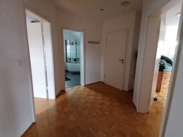 IMG_20250724_153325.jpg Flur in einer Wohnung mit Holzboden, Zugang zu Badezimmer, Schlafzimmer und einem weiteren Raum.