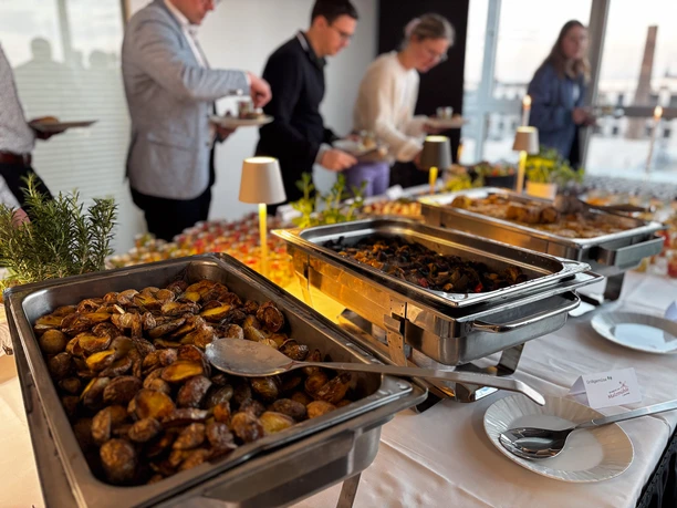 Business Buffet Catering Köln Reihe von Personen bedient sich an einem Buffet mit verschiedenen warmen und kalten Speisen.