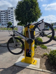 ADAC Station Bergneustadt Ein Fahrrad hängt in einer gelben ADAC-Radservice-Station. Im Hintergrund ist ein Baum und Wohnhäuser zu sehen.