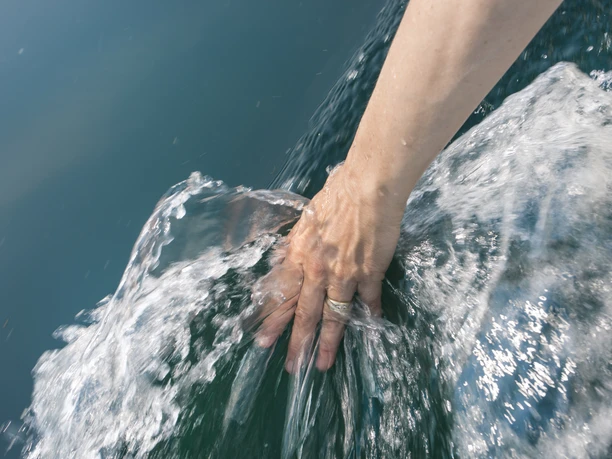 Cospudener See©Katja Fouad Vollmer (22).jpg Eine Hand berührt wellenförmig bewegtes, klares Wasser mit reflektierenden Lichtspiegelungen.
