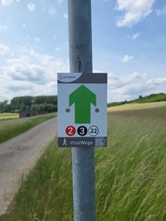 Beschilderung auf dem VitalWeg 2,3,22 Wegweiser des VitalWeg 2 in Einbeck mit grünem Pfeil und Nummernsymbolen auf Feldweg.