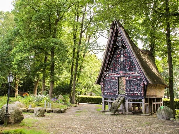 Batakhaus in Werpeloh ©Emsland Tourismus GmbH (3).jpg Pfahlhaus mit kunstvoll bemaltem Giebel und Reetdach, umgeben von alten Bäumen im Naturpark Hümmling