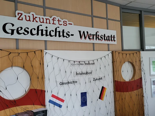 Geschichts- und Zukunftswerkstatt, Sögel ©Naturpark Hümmling (13).jpg Eingangsbereich der Geschichts- und Zukunftswerkstatt mit Infowand, Flaggen und Schriftzug an der Wand.