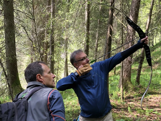 IMG_8530.jpg Ein Mann schiesst mit einem Pfeilbogen, während der Guide ihn beobachtet und kontrolliert.