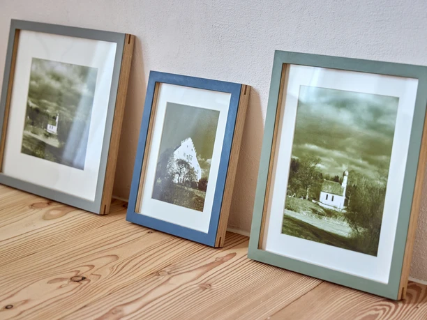 zr-ih-ndh25-064-marcgilsdorf.jpg Drei gerahmte Schwarz-Weiß-Fotografien auf einem Holzboden an einer Wand.