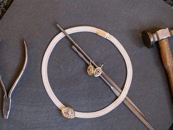 Goldschmiede Thomas Schwabe Halskette und Ohrringe aus Gold auf Schieferplatte, mit Hammer, Feilen und Zange.