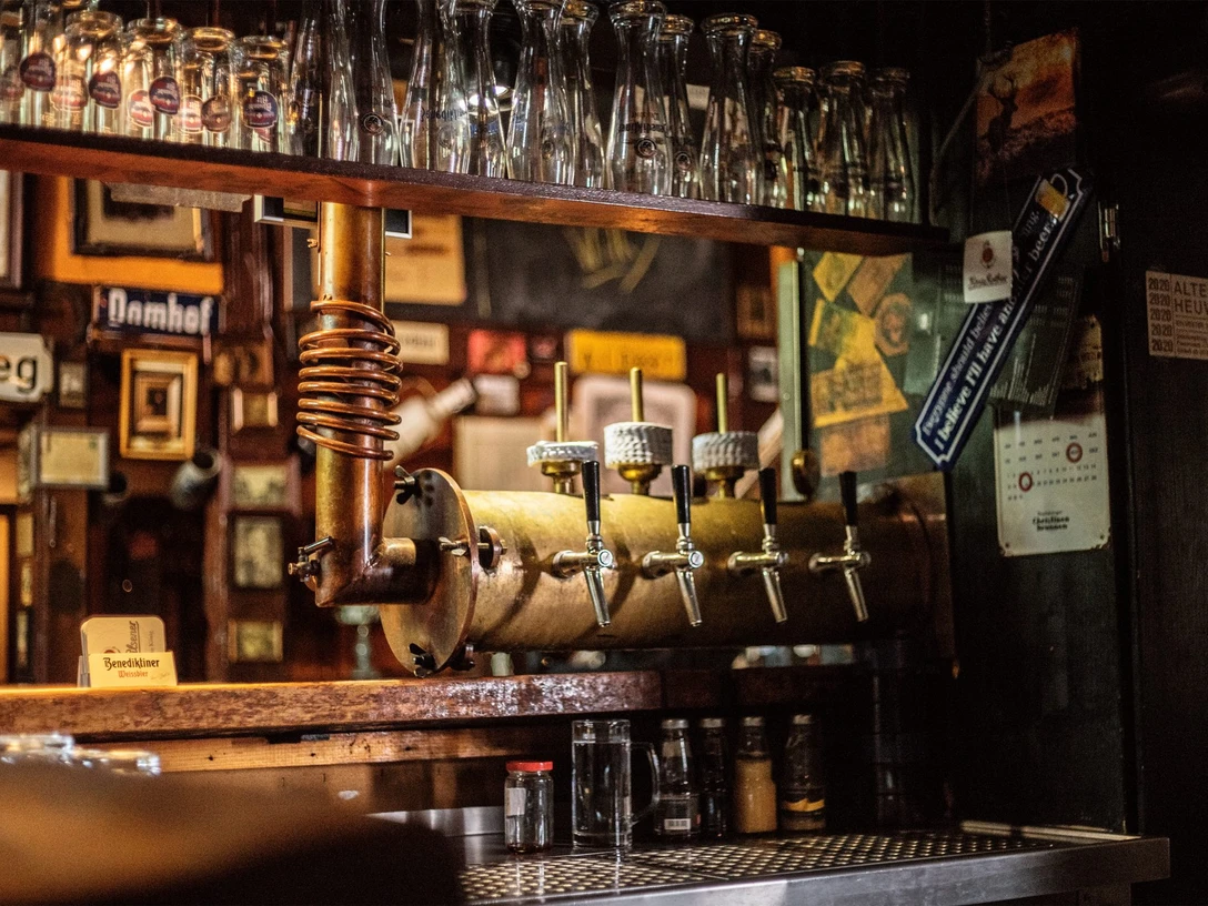 Kneipe Alte Heuwaage Gütersloh Historische Zapfanlage mit mehreren Hähnen, darüber Reihen sauberer Biergläser an der Theke.