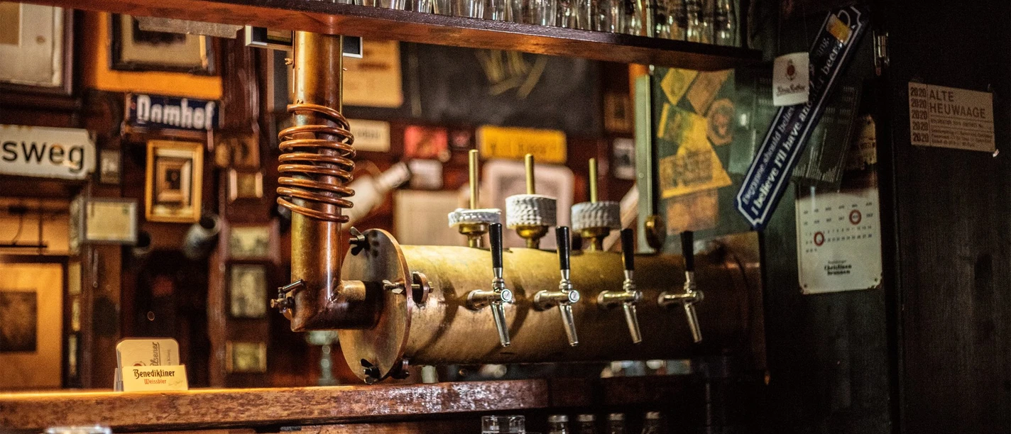 Kneipe Alte Heuwaage Gütersloh Historische Zapfanlage mit mehreren Hähnen, darüber Reihen sauberer Biergläser an der Theke.