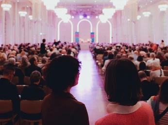 lit.COLOGNE Blick auf einen eleganten, festlich beleuchteten Saal, gefüllt mit aufmerksam lauschenden Menschen.View of an elegant, festively lit hall, filled with people listening attentively.