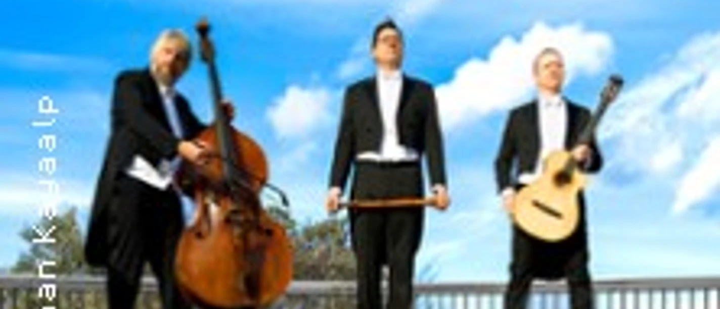 Drei Musiker in eleganten Anzügen, posieren mit Kontrabass, Gitarre und Cello vor blauem Himmel.