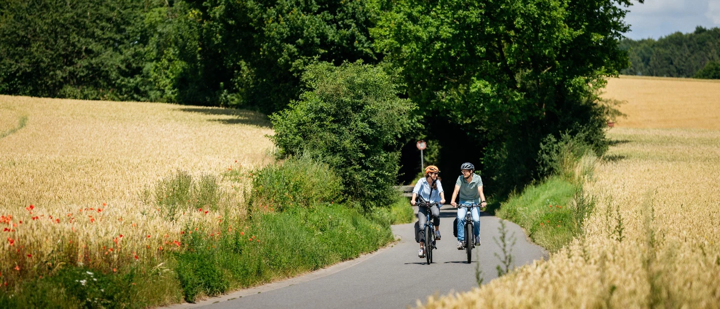Zwischen Hasbergen und Hagen a.T.W. Zwei Radfahrer auf einer ländlichen, von Feldern gesäumten Straße an einem sonnigen Tag.