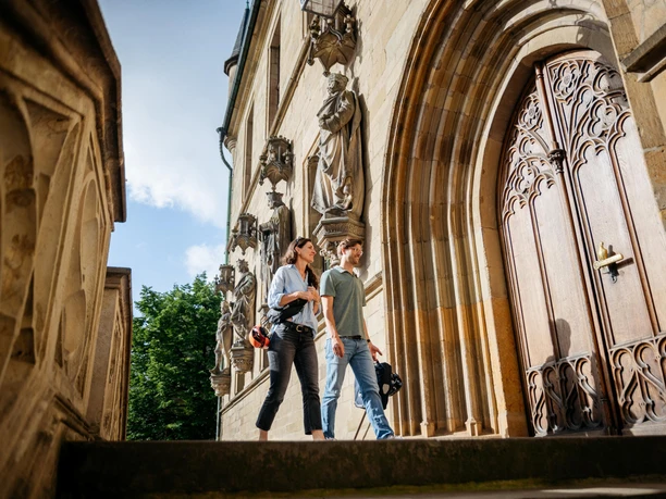 Am Historischen Rathaus Osnabrück Zwei Personen vor dem reich verzierten Portal des Historisches Rathaus Osnabrück, mit gotischer Fassade und steinernen Figuren.
