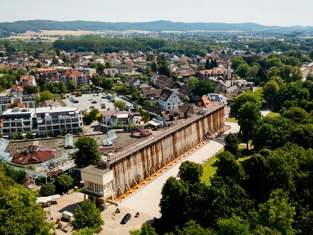 Gradierwerk in einer grünen Parklandschaft, umgeben von Stadthäusern und Hügeln im Hintergrund.