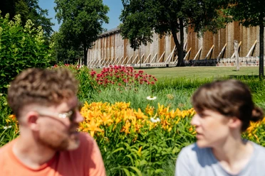 bad-rothenfelde-grenzgaengerroute-copyright-tol-foto-christoph-steinweg (3).jpg Zwei Personen vor einem alten Gradierwerk mit blühendem Garten im Vordergrund.