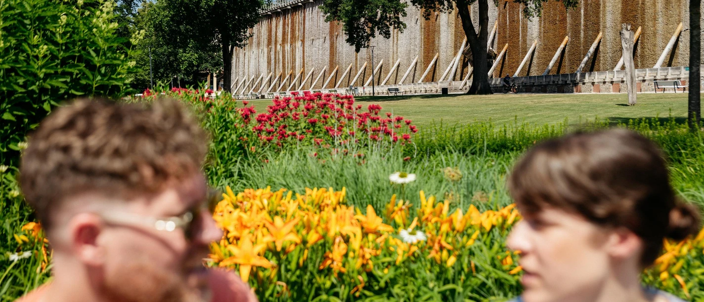 bad-rothenfelde-grenzgaengerroute-copyright-tol-foto-christoph-steinweg (3).jpg Zwei Personen vor einem alten Gradierwerk mit blühendem Garten im Vordergrund.