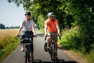 Mit dem Rad unterwegs in der Radregion Osnabrücker Land Zwei Radfahrer auf einem asphaltierten Weg im Grünen, lächelnd unterwegs.
