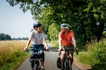 Genießen beim Radfahren im Osnabrücker Land Zwei Männer auf Fahrrädern lachen und fahren auf einem ländlichen Weg entlang.