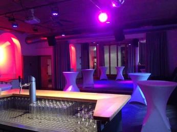 Eigelsteintorburg Bar Ein stilvoller, minimalistischer Veranstaltungsraum mit Stehtischen, sanft beleuchtet in violetten Tönen.A stylish, minimalist event room with bar tables, softly lit in purple tones.