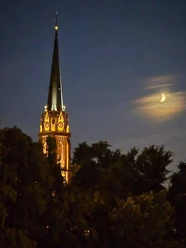 Erleuchteter Kirchturm und Mondsichel bei Nacht.