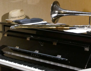 Jazzmusik Auf einem geschlossenen Klavier liegt ein Hut neben einer Trompete und Noten; Musikinstrumente im Fokus.