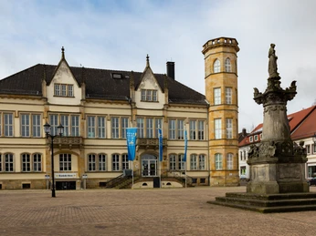 10235-Rathaus-2016_ © Werner Wilmes.jpg Historisches Gebäude mit grauem Dach, Zierbalkonen und Turm. Platz mit Steinbrunnen im Vordergrund.